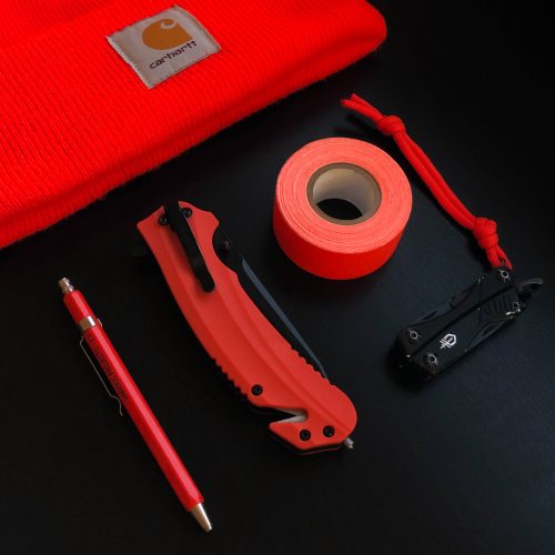 everyday carry flatlay of safety orange beanie, pencil, knife, gaff tape, and multitool