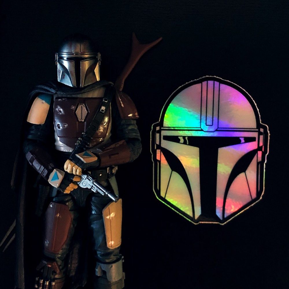 Mandalorian action figure next to a holographic sticker of a mandalorian helmet